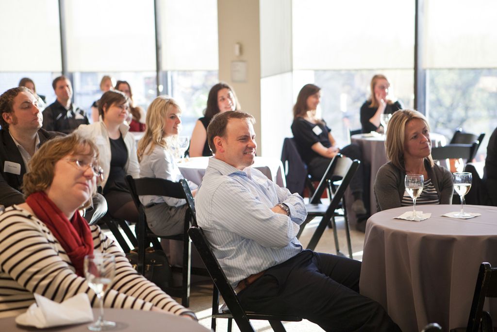 A group of adults sit in chairs and look towards a speaker.