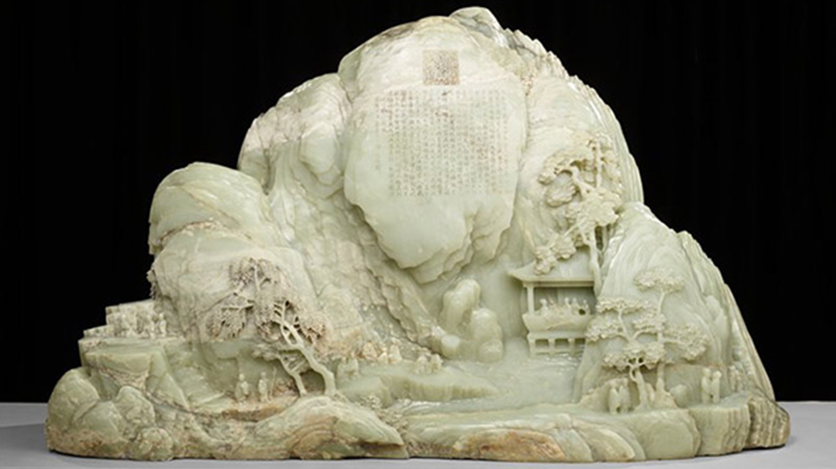 Jade carving of mountainous landscape that includes trees, people, and buildings.
