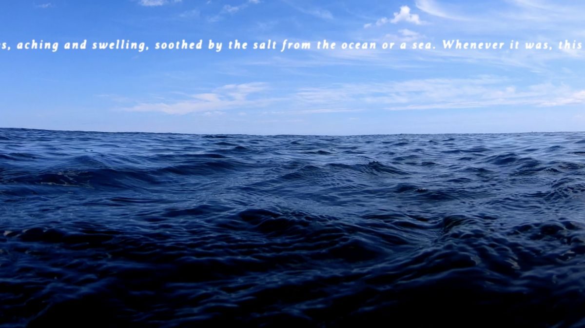 A mass of blue water takes up the lower half of the screen while text is set against a blue sky with wispy clouds passing by. The visible text reads, “aching and swelling, soothed by the salt from the ocean or sea. Whenever it was, this...”