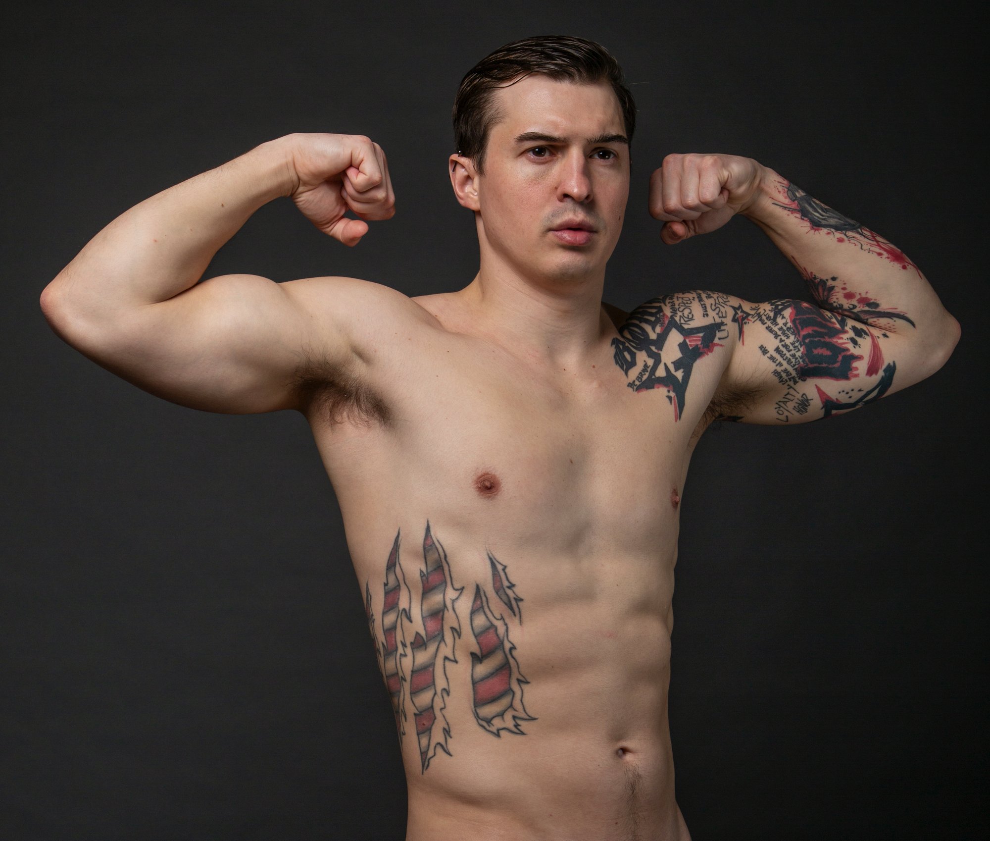 A tattooed man who is slender yet muscular appears to flex his arms.