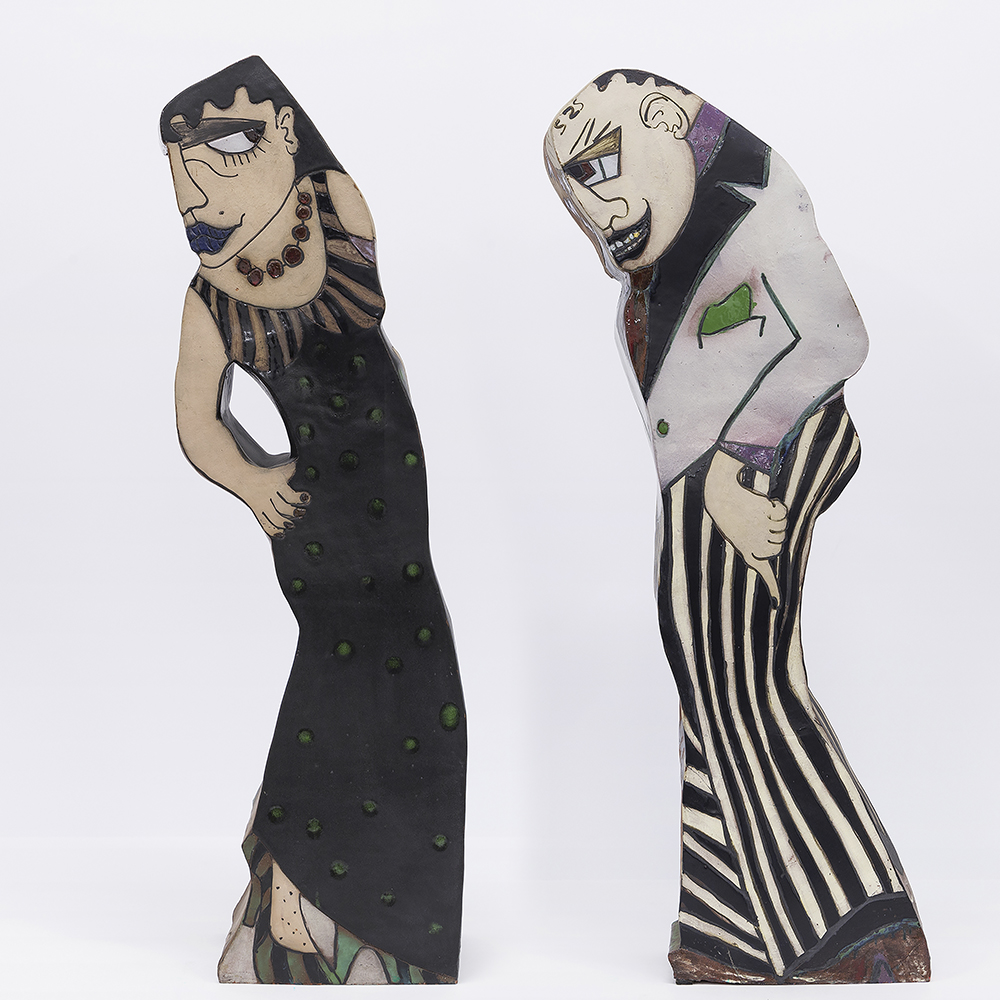 These are two ceramic sculptures of a couple by Camille Billops. The woman is wearing a black dress with green detailing while the man is wearing gray suit coat and striped dress pants.