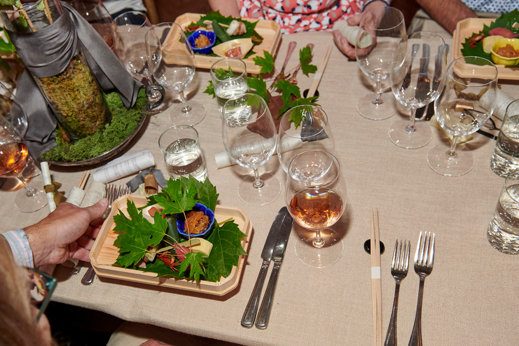 A banquet dinner table filled with glass cups, silverware and a Japanese meal.