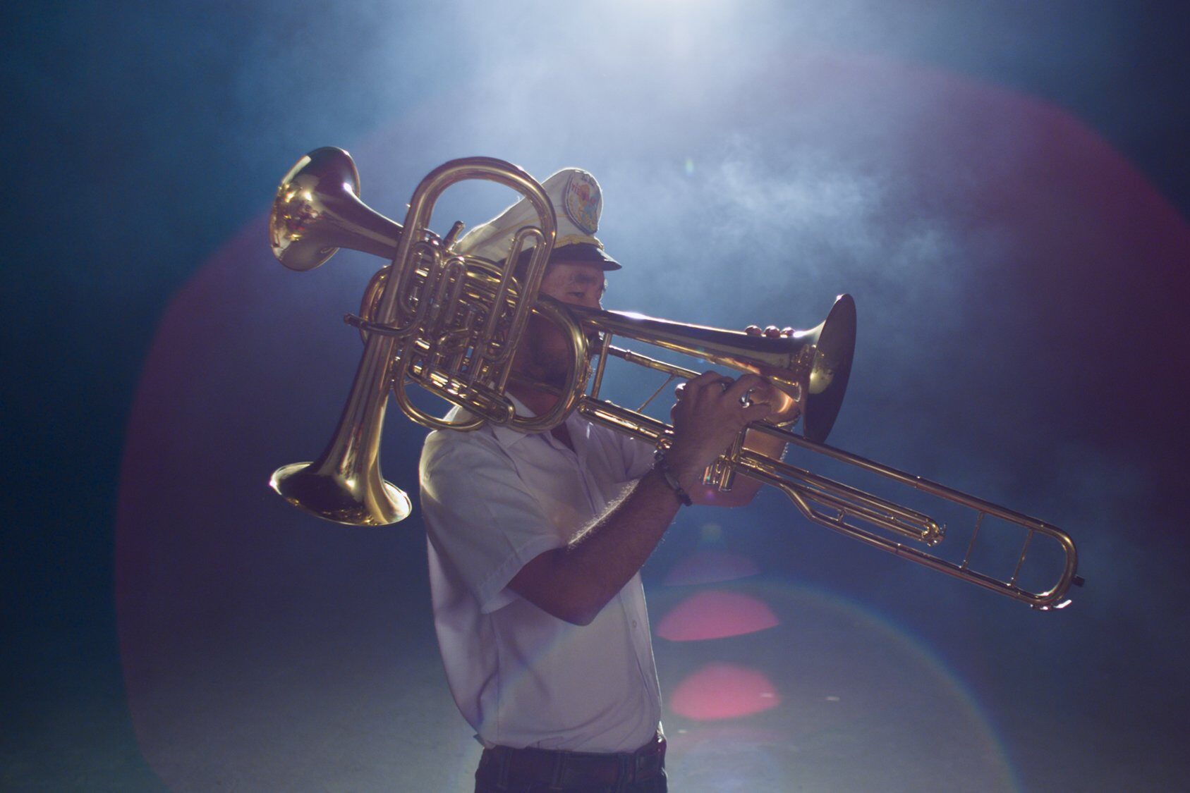 A overhead light shines above a trombone player in a band uniform.
