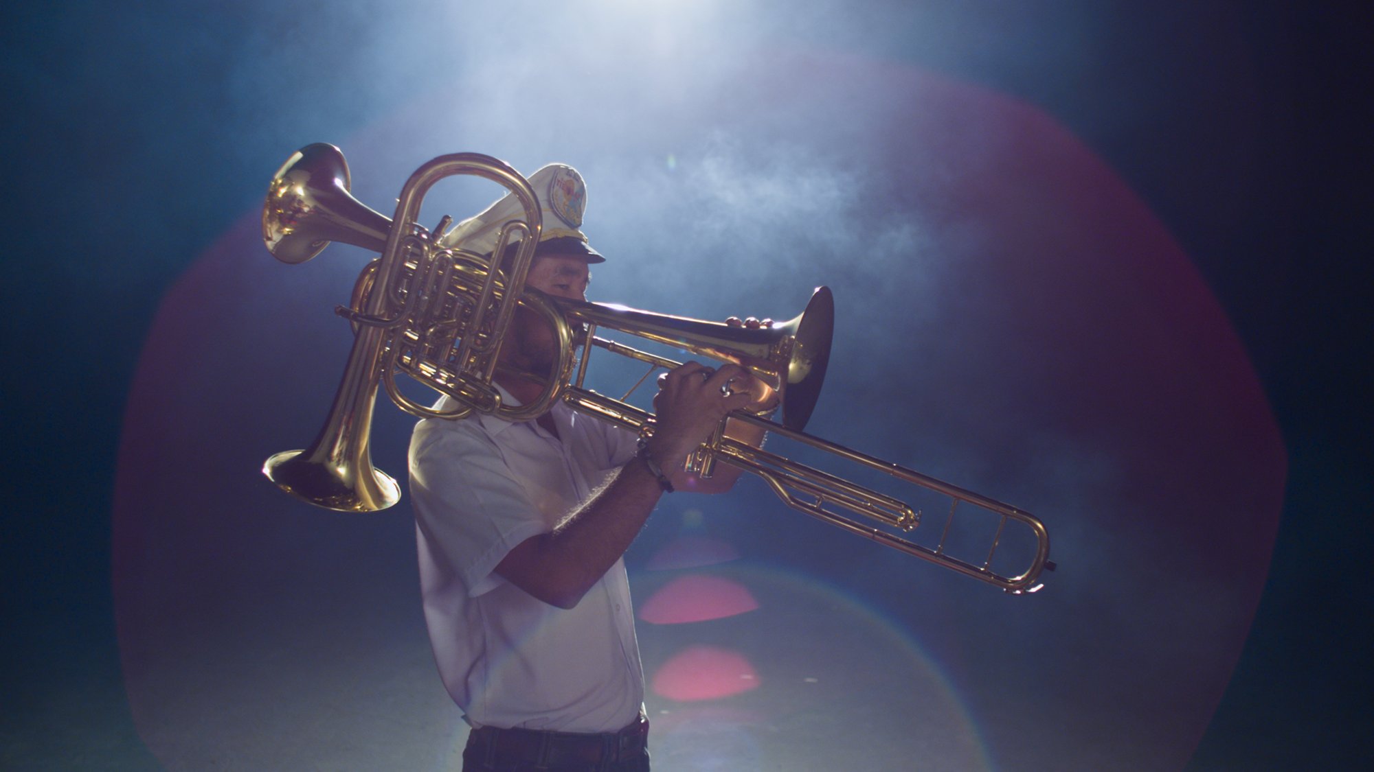 A overhead light shines above a trombone player in a band uniform.