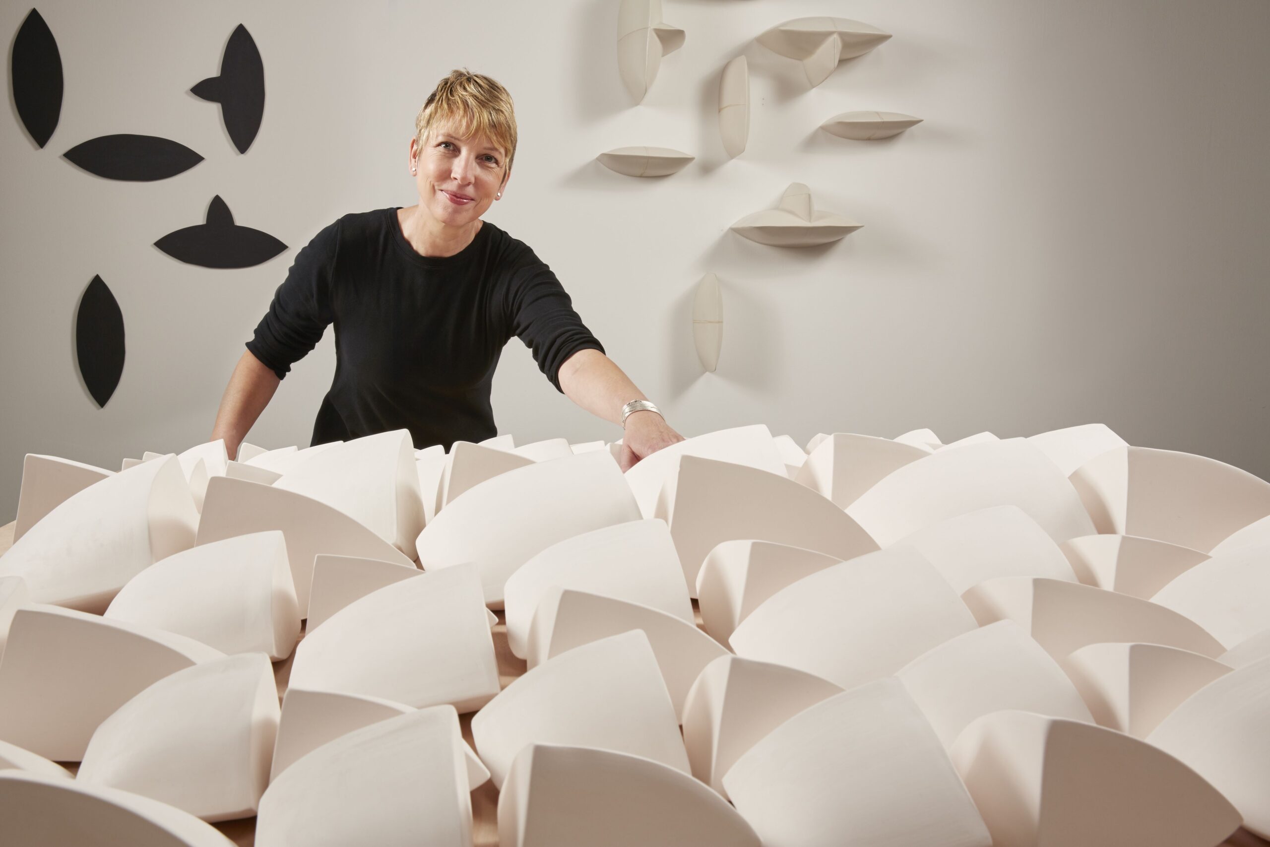 A person in all black looks towards the camera while standing behind their latest artwork.