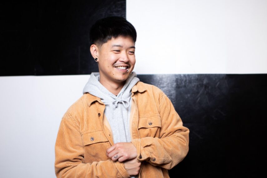 Person in tan jacket standing in front of black and white wall.