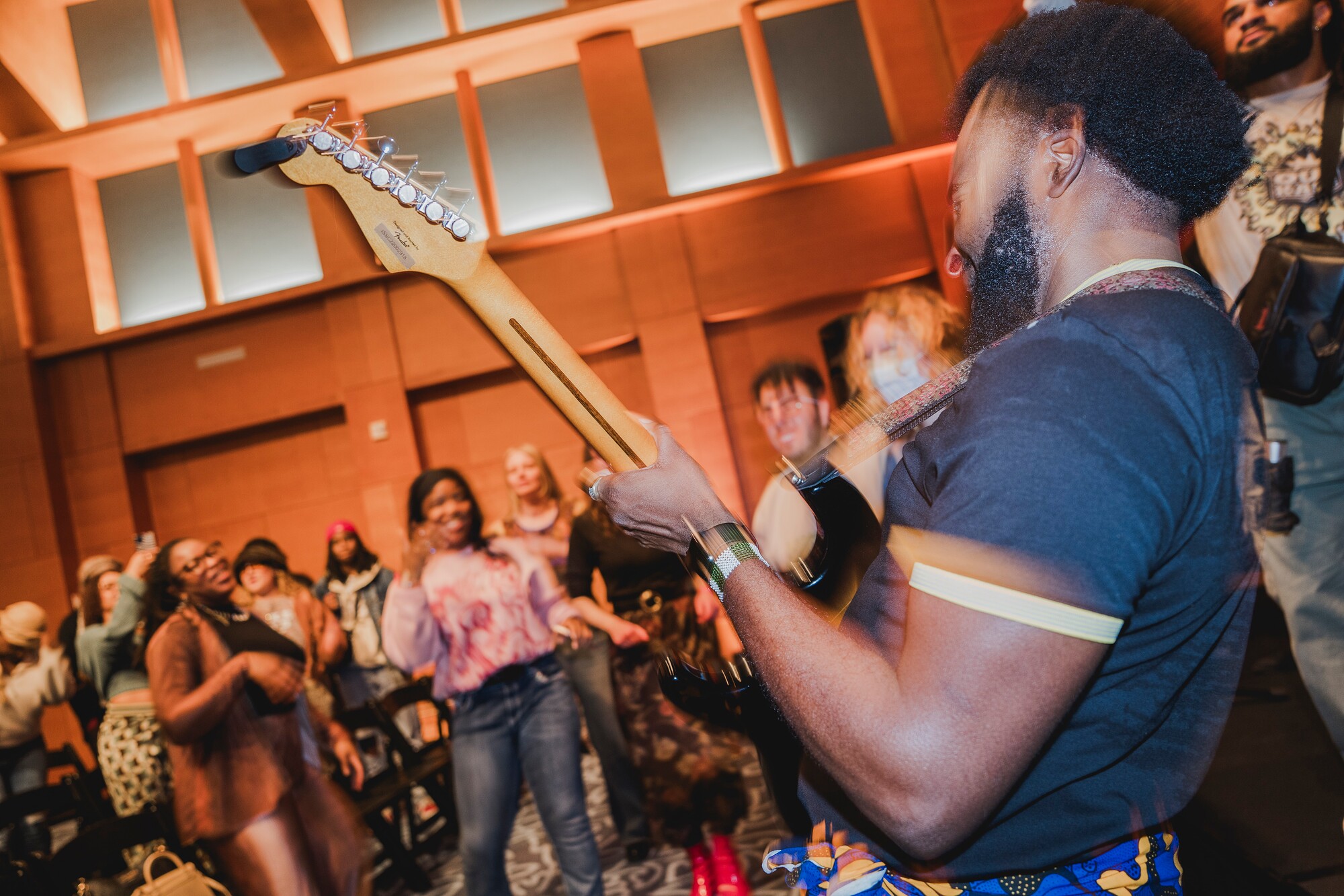 Musician playing guitar in front of a lively crowd indoors.