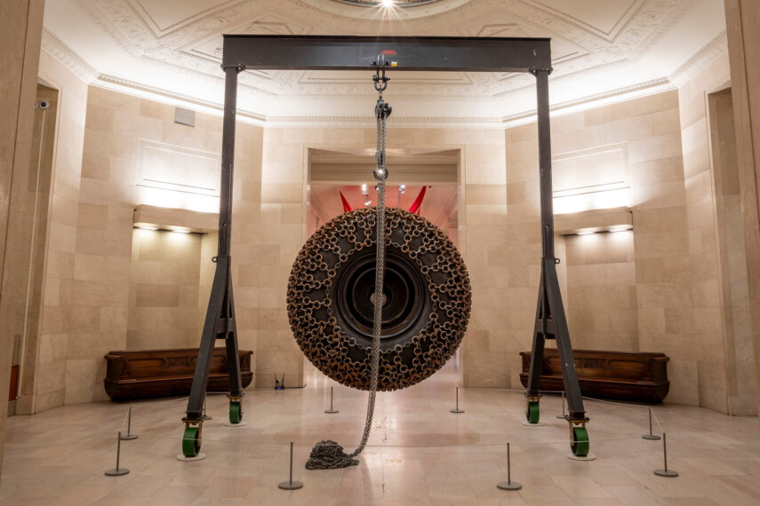 Sculpture of a large circular object suspended from steel beams