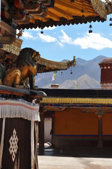 view of the mountains from the Jokhang Temple Monastery in Tibet, framed by golden eaves of the temple and a lion on a pedestal 