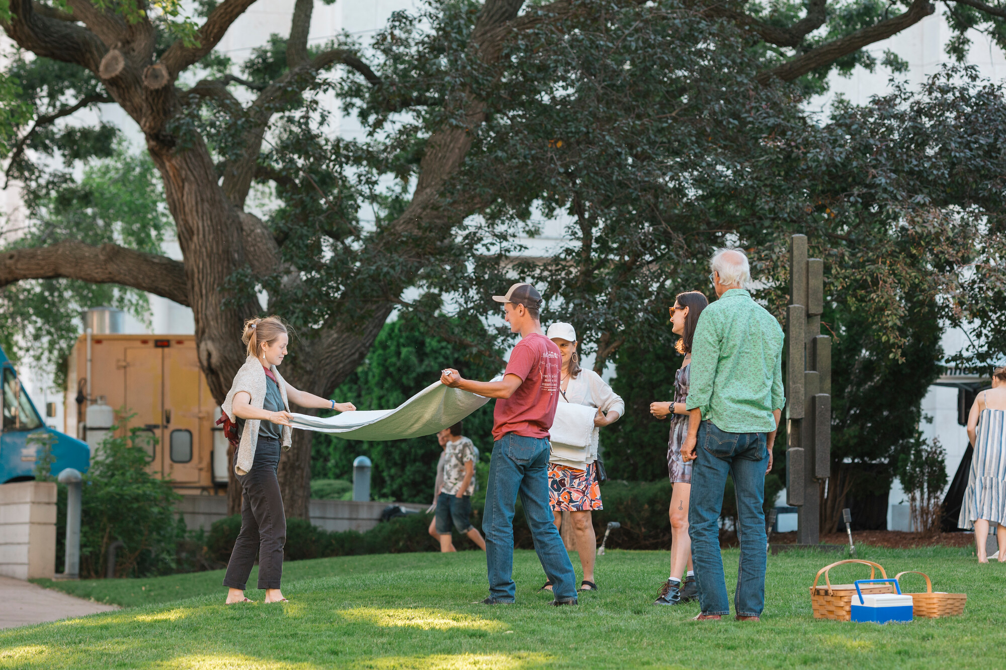 People with picnic baskets laying out a blanket on the lawn