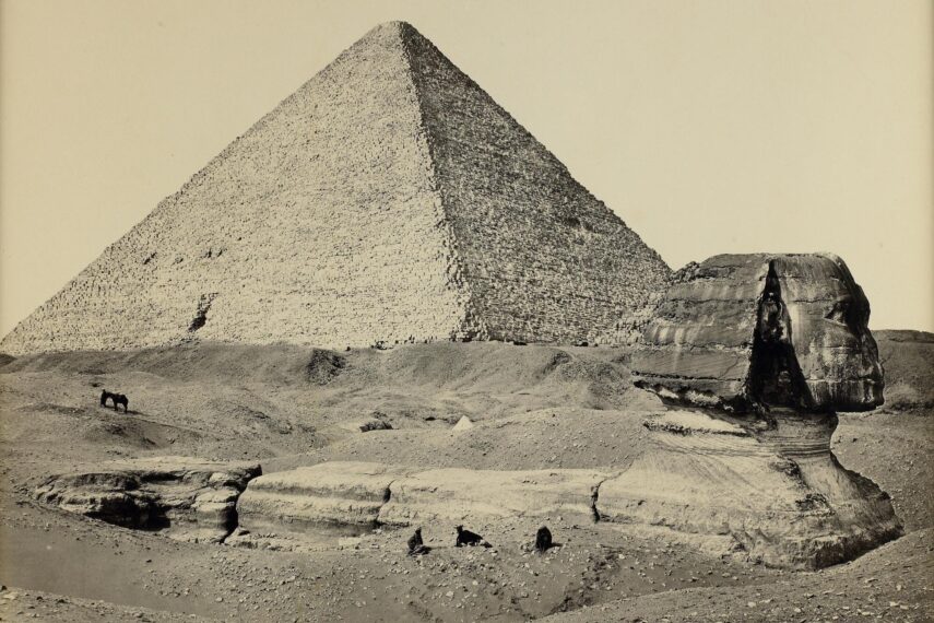 Photograph of the Sphinx, partially excavated, in the foreground and one of the great pyramids in the background