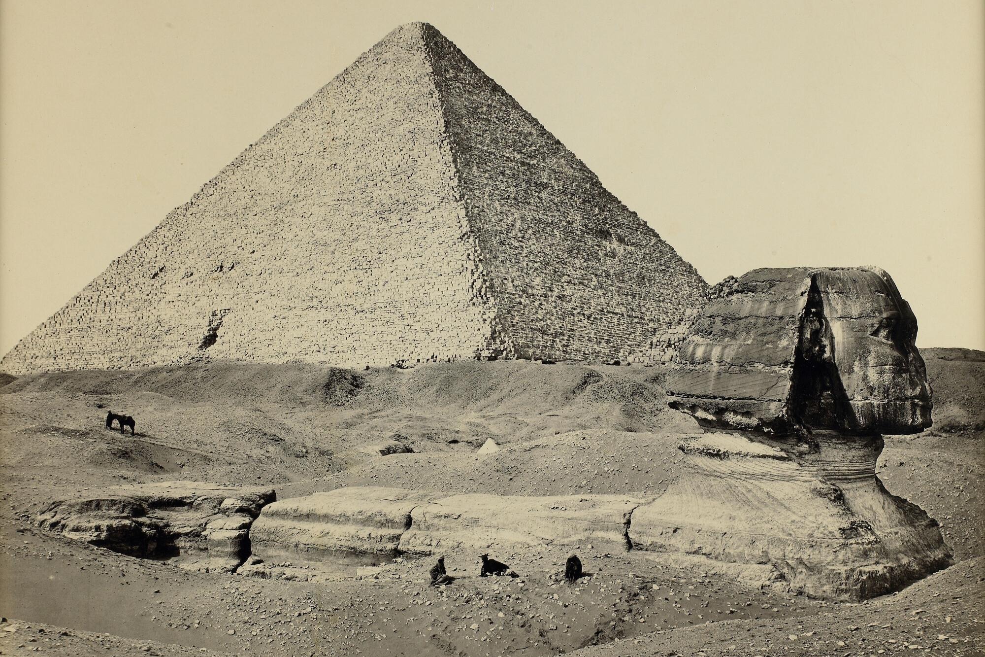 Photograph of the Sphinx, partially excavated, in the foreground and one of the great pyramids in the background