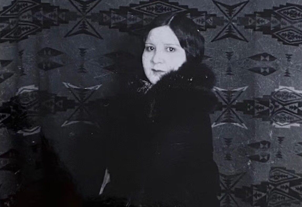 Black-and-white photograph of Mary Sully standing in from of a Dakota blanket
