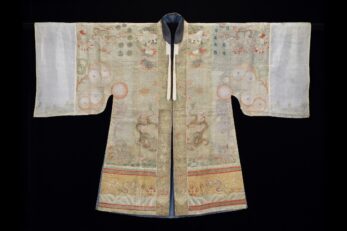 Photograph of an outstretch Daoist robe with long sleeves, with white fabric at the cuffs and beige fabric with orange, yellow, and brown embroidery on the body