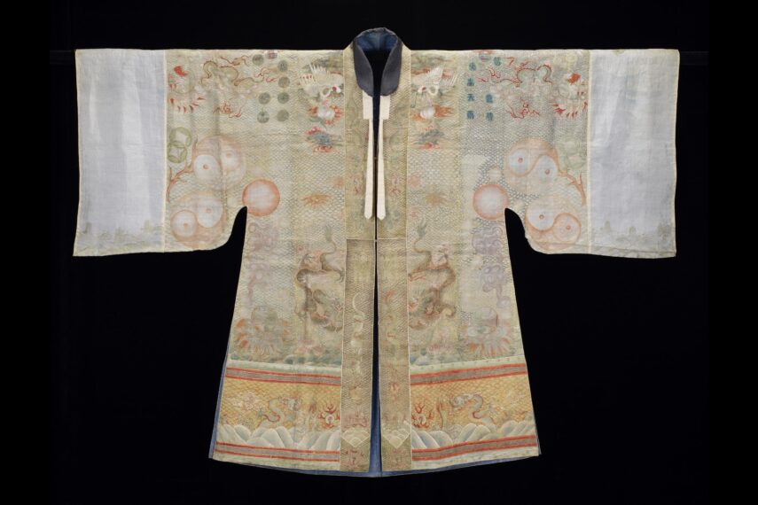 Photograph of an outstretch Daoist robe with long sleeves, with white fabric at the cuffs and beige fabric with orange, yellow, and brown embroidery on the body