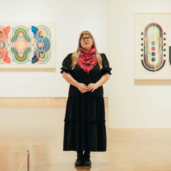 Photo of Tia Keobounpheng in a Mia gallery standing in front of her colorful embroidered tapestries