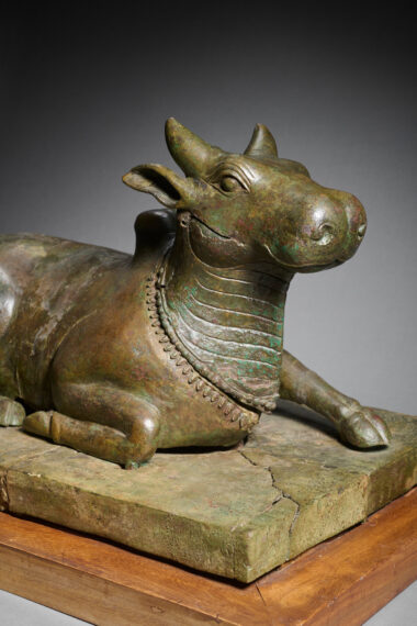 Bronze statue of bull lying on its stomach, head held upright