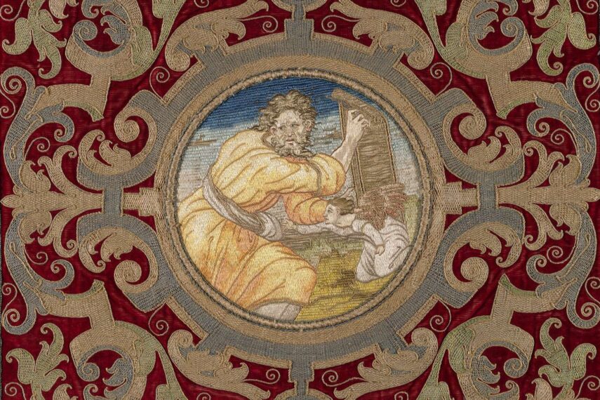Tapestry with the central roundel of Saint Matthew holding the gospel in the form of a scroll with a diminutive kneeling angel, set against a verdant landscape and blue sky; framed by elaborate goldwork embroidery