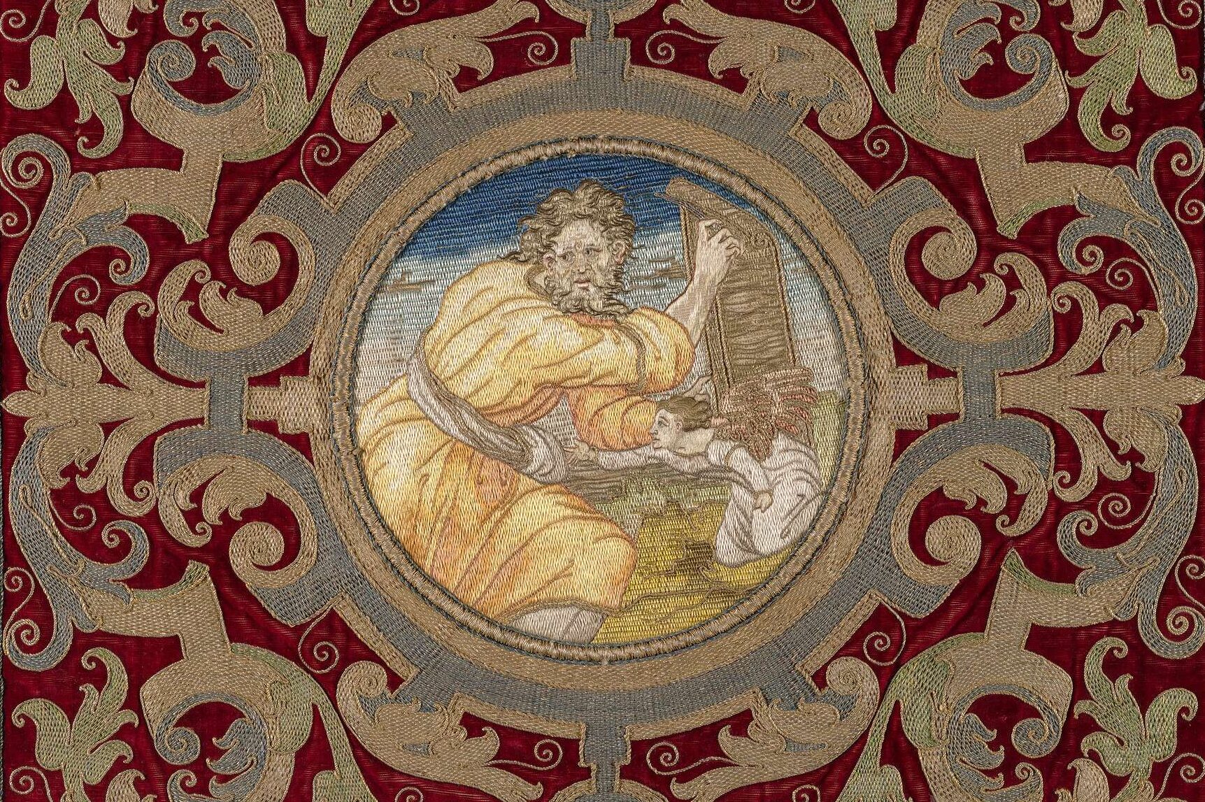 Tapestry with the central roundel of Saint Matthew holding the gospel in the form of a scroll with a diminutive kneeling angel, set against a verdant landscape and blue sky; framed by elaborate goldwork embroidery