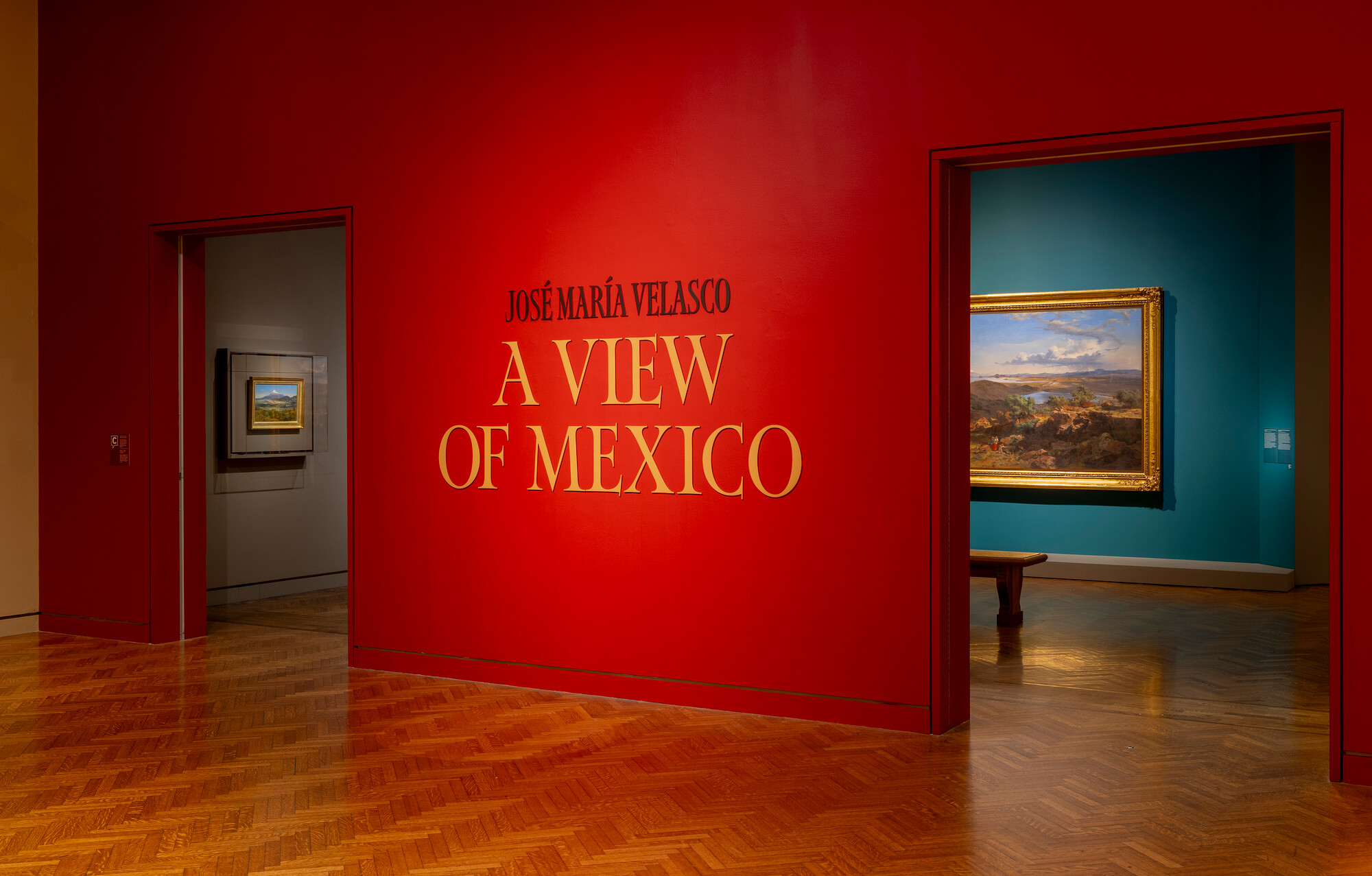 View of the entrance to the Velasco exhibition, with a bright red wall on the exterior and teal-colored walls showcasing the paintings inside the exhibition