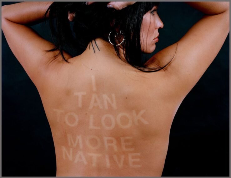 Photo of a woman's bare back with the words "I tan to look more native" written on her back in reverse color to look like tan lines