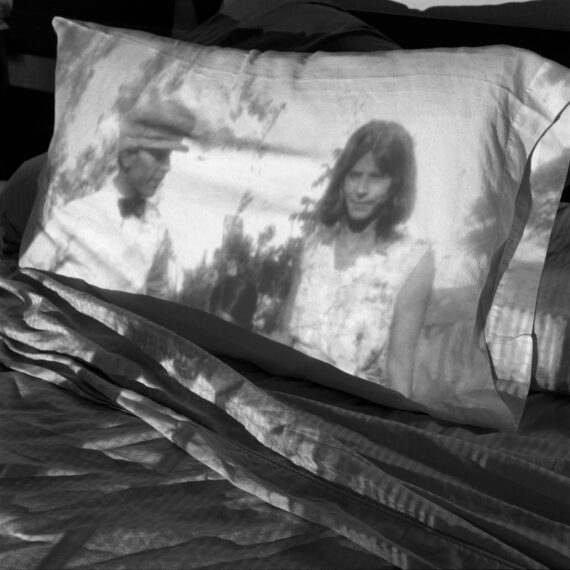 Black-and-white photograph showing an image of a man and a woman projected onto a pillow resting on a rumpled bed.