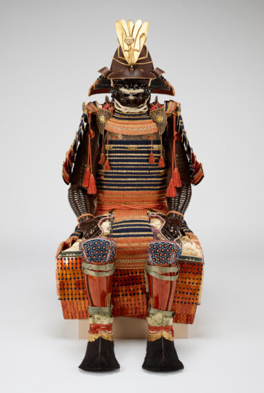 suit of armor displayed in a sitting position includes helmet with praying mantis forecrest, face mask, torso covering, pair of front shoulder medallions that attach to torso covering, pair of large upper arm guards, pair of small shoulder coverings, pair of gauntlets with arm and hand guards, apron, pair of leg guards, and pair of boot coverings
