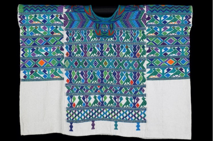 Three panel huipil; elaborate embroidery encircles the neck; white ground cloth with patterning primarily in green with accents in purple, blue, orange and red; design consists of rows of stylized bird and tree pattern alternating with rows of diamonds