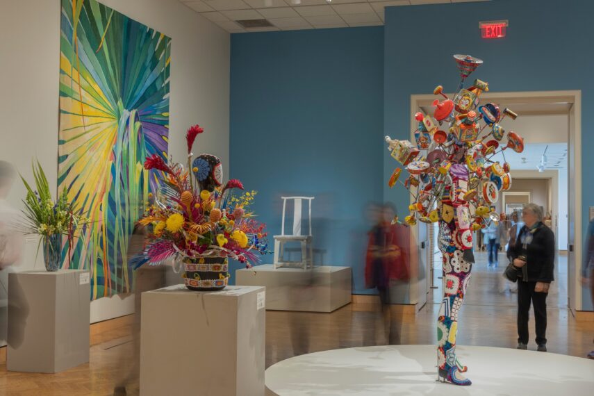 View of a gallery with a painting on the wall and a floral arrangement interpretation next to it.