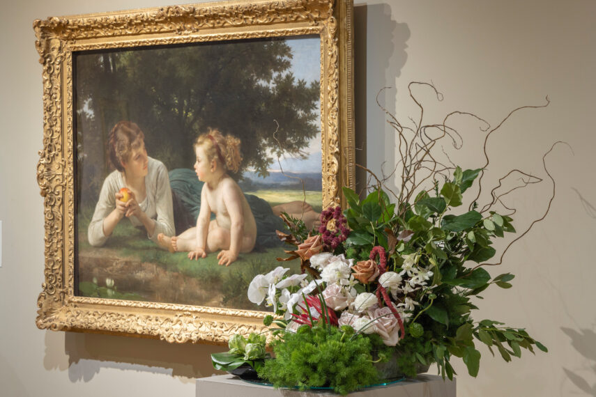 View of a gallery with a painting on the wall and a floral arrangement interpretation next to it.