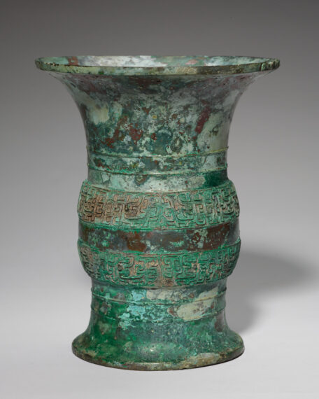 Ancient bronze vase with intricate patterns and green patina. The vase has a flared mouth and a slightly wider base, tapering in the middle.