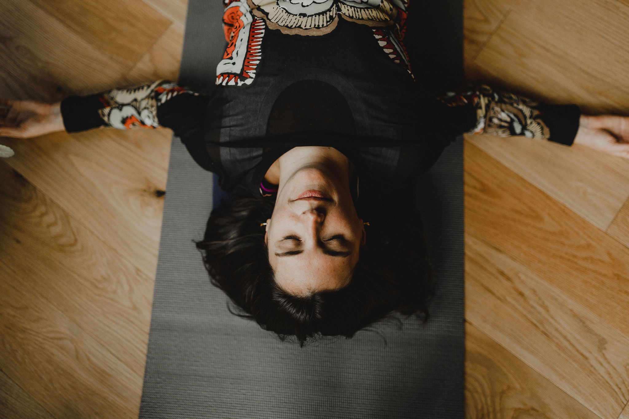 Woman with her eyes closed lying upside down on a black yoga mat