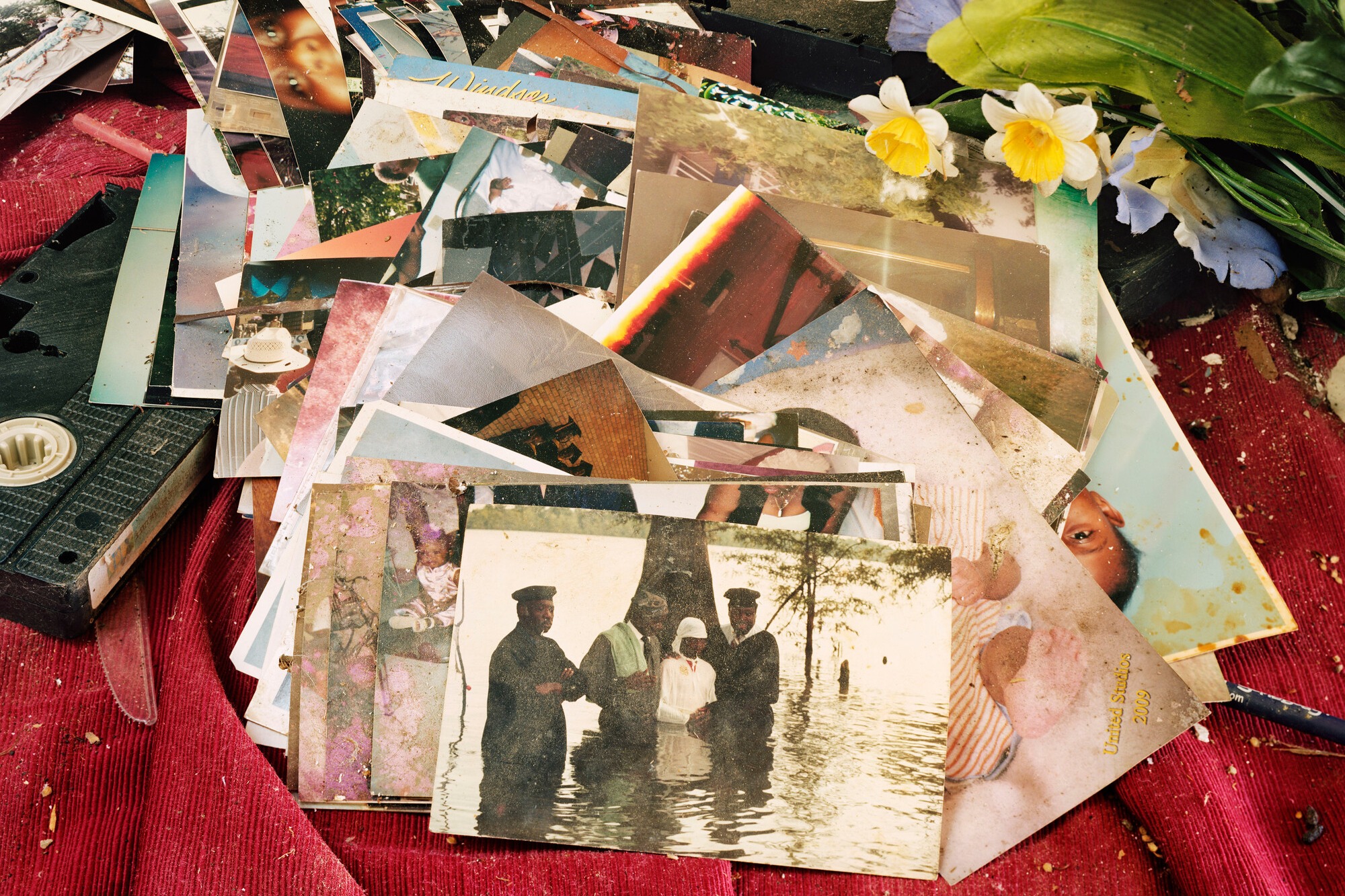 A pile of old, somewhat worn photographs scattered over a textured red fabric background