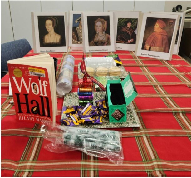 Display of the book "Wolf Hall," snacks, and paintings on a red plaid tablecloth.