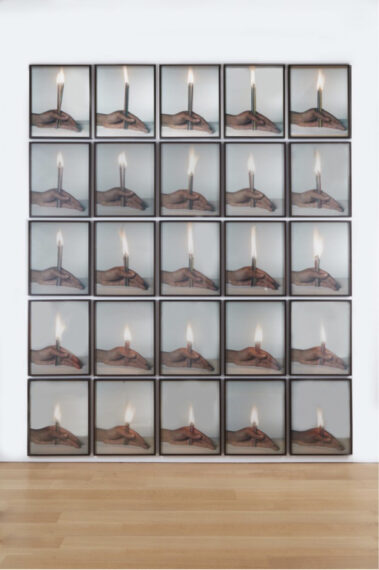The image shows a grid composed of framed photographs arranged in five rows and five columns, totaling 25 individual images. Each photograph features a hand holding a lit candle against a neutral background. The candle is vertically positioned, with the flame clearly visible at the top.
