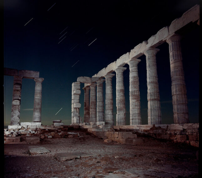 Ancient stone columns under a night sky with star trails.