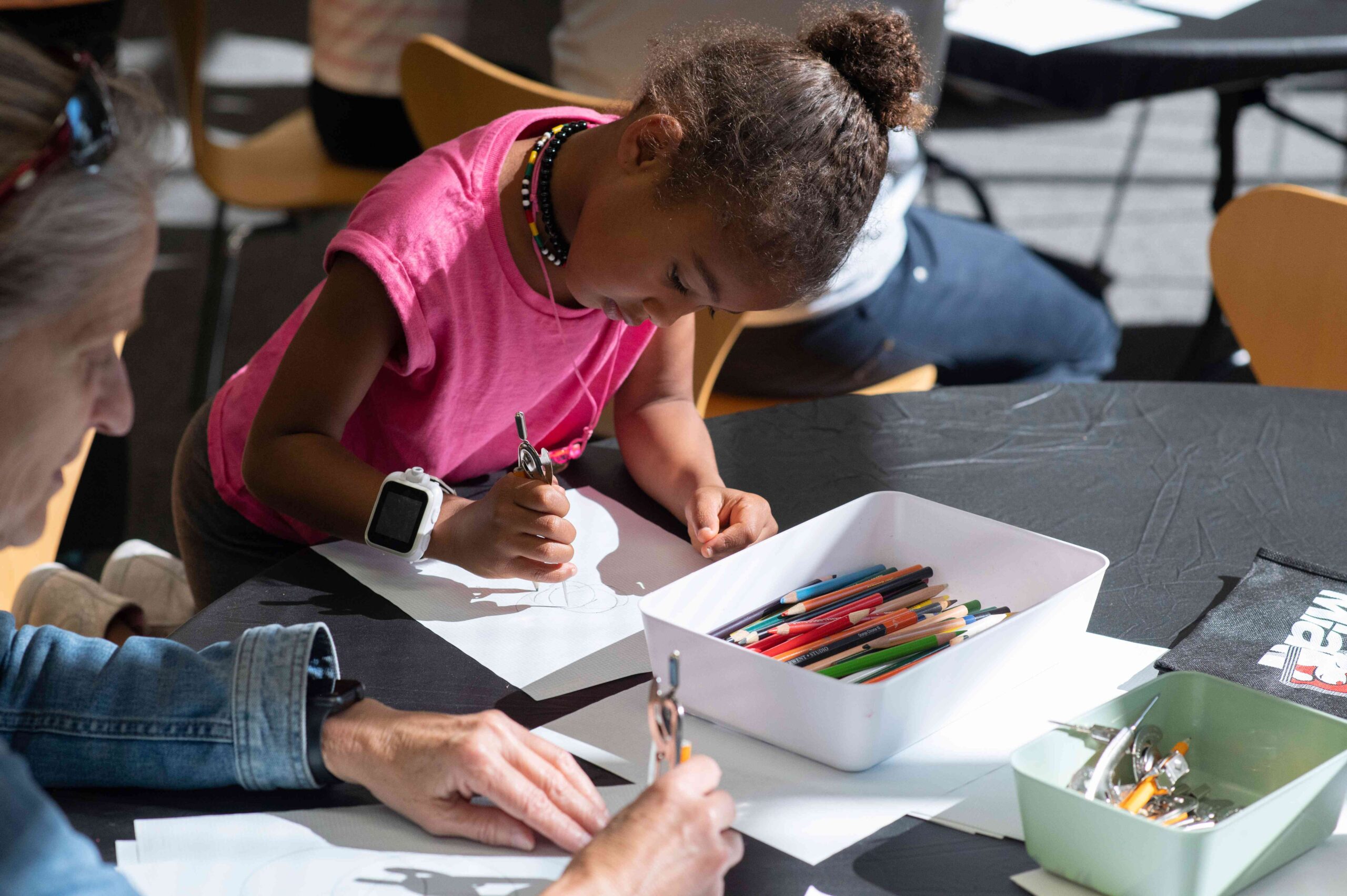 Young child drawing with colored pencils at a table.