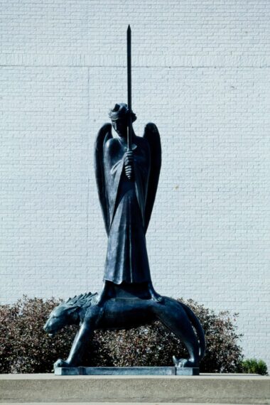 Outdoor statue of a winged figure holding a spear, standing on a lion.