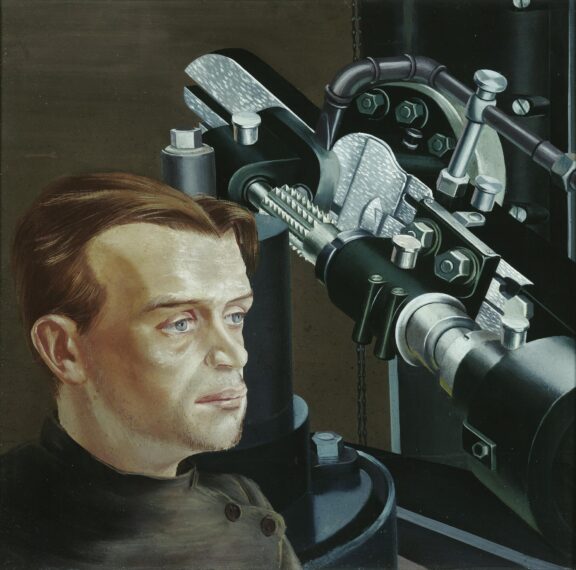 The image depicts a man with light brown hair and a fair complexion, framed in front of industrial machinery.