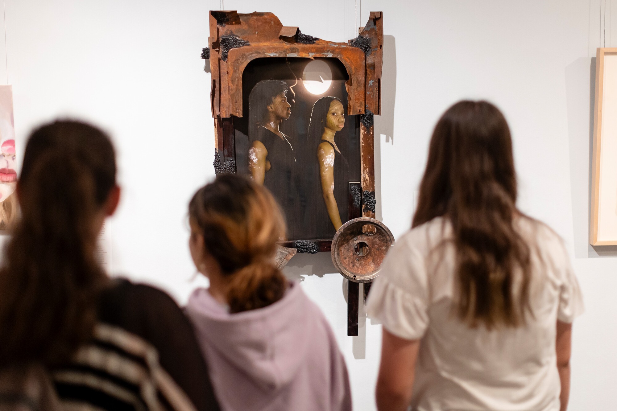 People viewing a mixed media artwork featuring two figures.