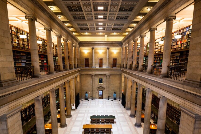 Interior of a large library with tall columns and two levels of bookshelves.