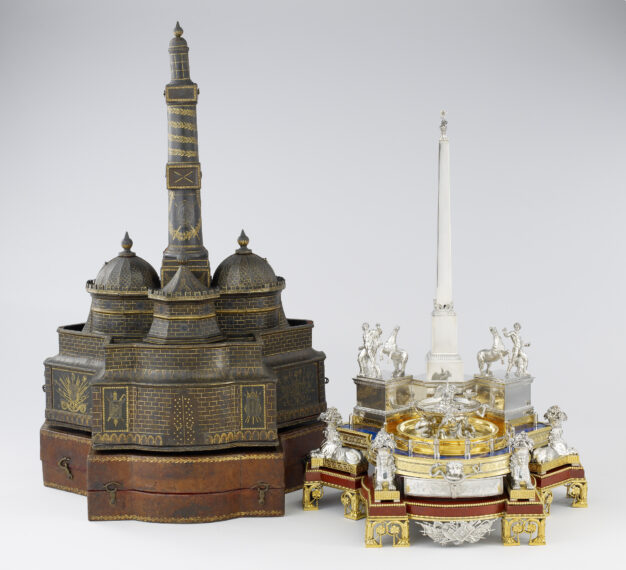 Two ornate architectural models, one dark and domed and the other silver and gold with figures.