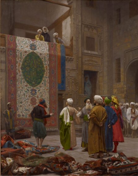 Painting of a busy scene in an ornate courtyard where several people dressed in traditional Middle Eastern attire are gathered. Various richly patterned carpets are scattered around them and above them a large carpet with intricate designs is draped over a balcony.