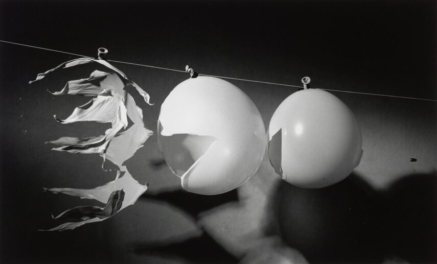 Black-and-white photograph of two balloons and a torn piece of material hanging on a wire.