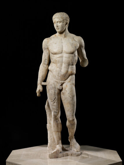 Marble statue of a male figure with muscular definition set against a dark background.