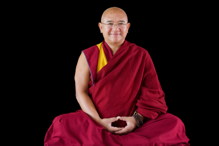 Monk in red robe sitting cross-legged against a black background