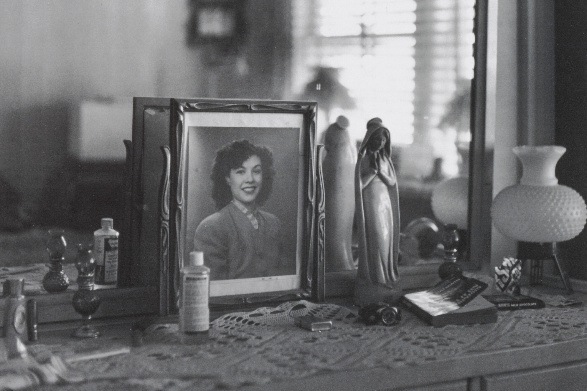 Black and white photo of a dresser with a portrait, bottles, and figurine