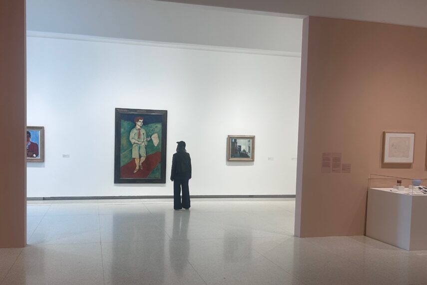 Photo of a person standing in an art gallery, looking at several paintings displayed on a wall.