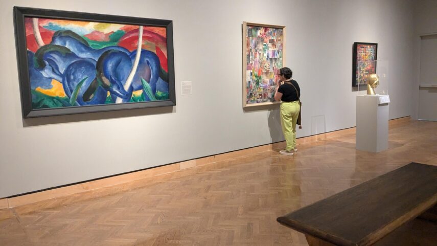 Photo of a person standing in an art gallery, closely observing a colorful abstract painting.