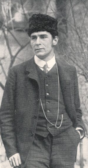 Black-and-white photo of a man in a vintage suit with a fur cap, standing outdoors.
